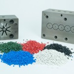 2 plastic extrusion molds behind green, red, blue, black, and white polymeric compounds
